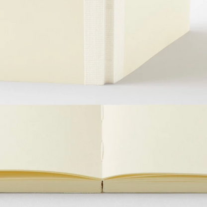 A close-up product photo of a cream-colored notebook or journal, showing the spine, page edges, and open spread of the pages against a clean white background.