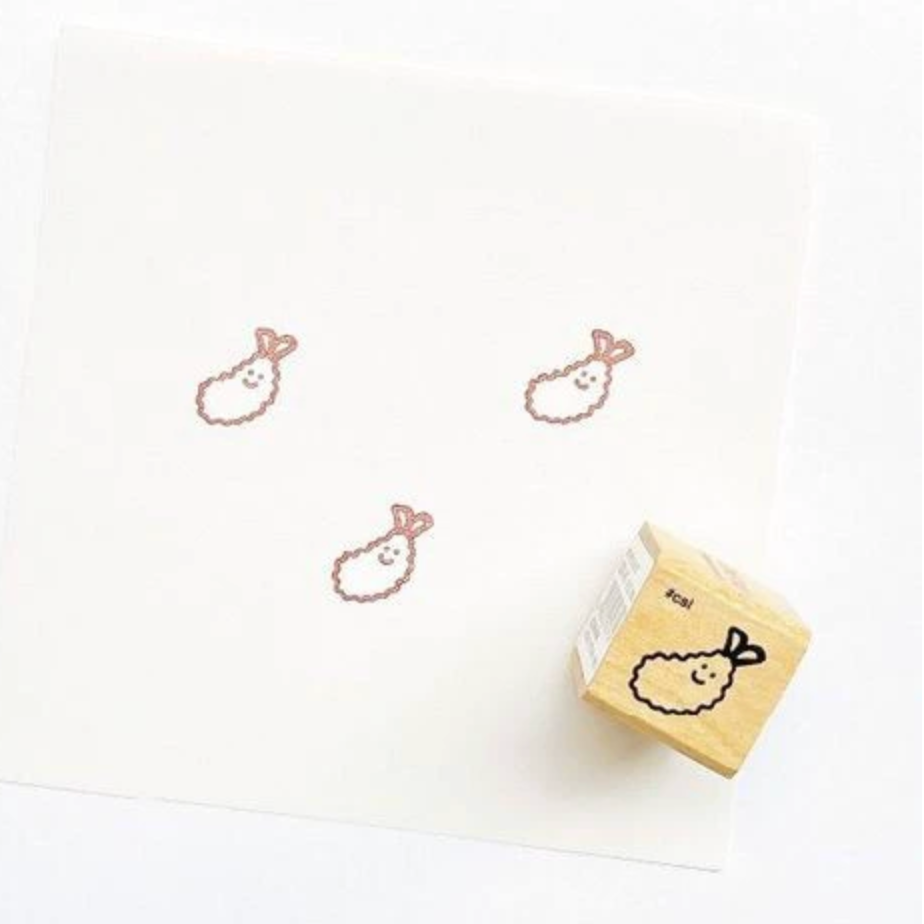 A wooden rubber stamp with a cute Rampo rabbit design, shown next to a white sheet of paper that features three stamped impressions of the same design.