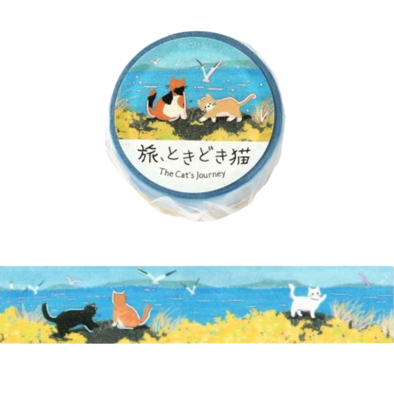 A roll of decorative washi tape with an illustrated coastal scene featuring three cats on a yellow beach under a blue sky, shown both as a circular top view and a narrow horizontal strip.