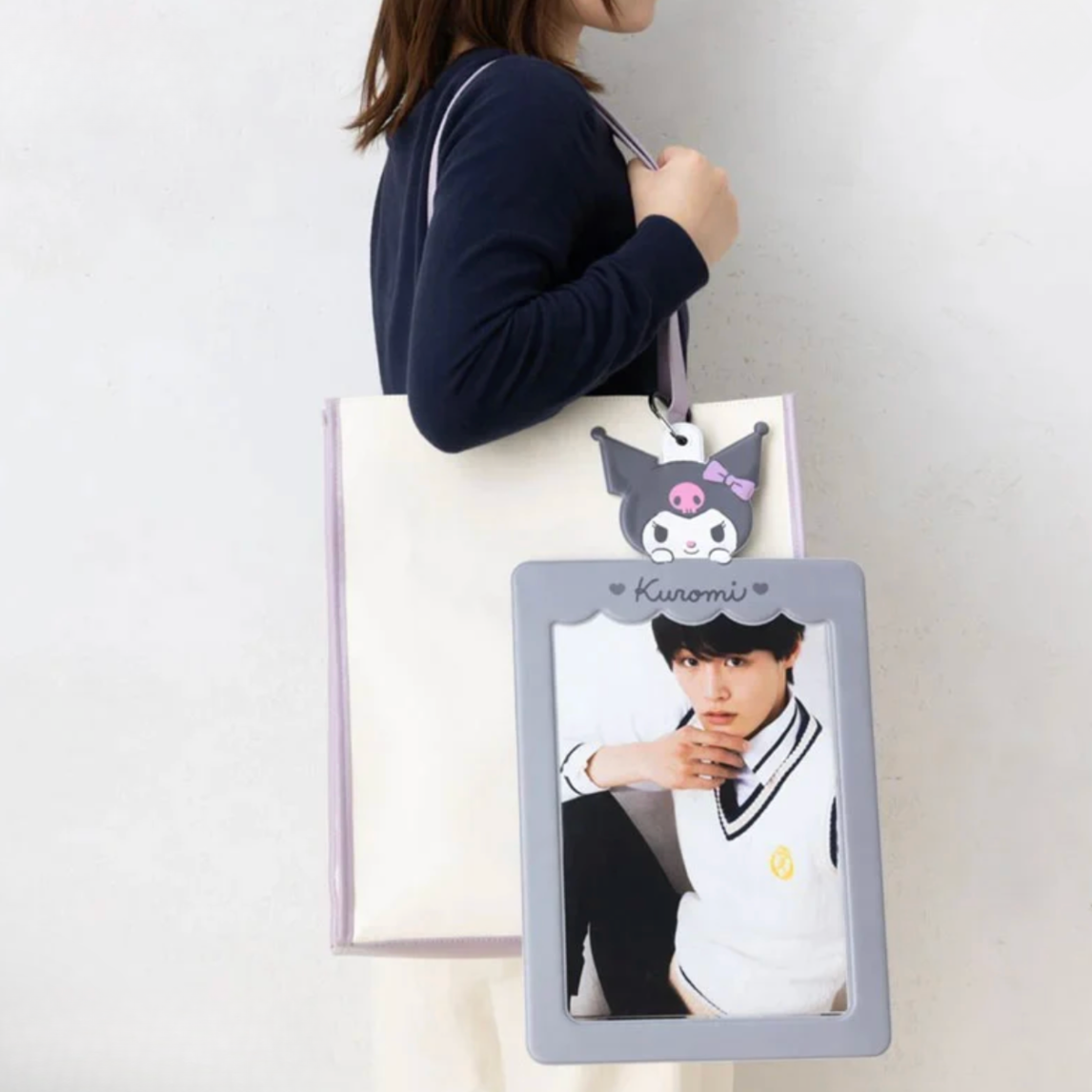Person holding a tote bag with a character design and photo of a person on a gray frame.