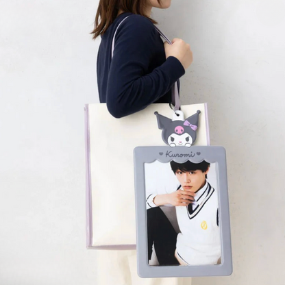 Person holding a tote bag with a character design and photo of a person on a gray frame.