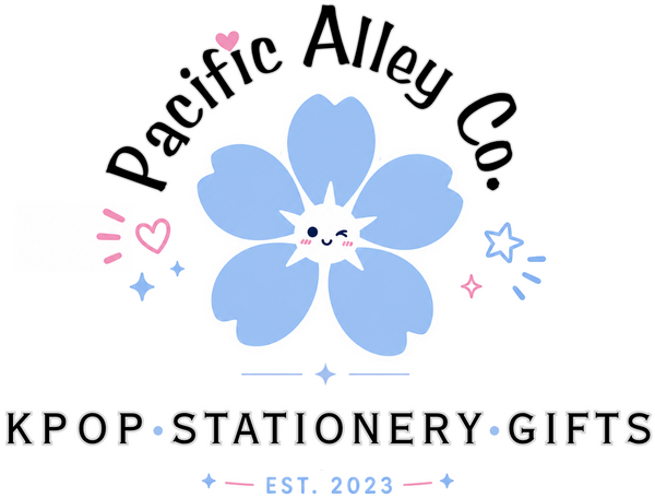 Logo for Pacific Alley Co. featuring curved black text above a large, cute blue flower with five rounded petals and a smiling face in the center. Small pink hearts and blue star doodles surround the flower. Below, the text reads "KPOP - Stationery - Gifts" and "EST. 2023" in soft blue and pink accents on a white background.