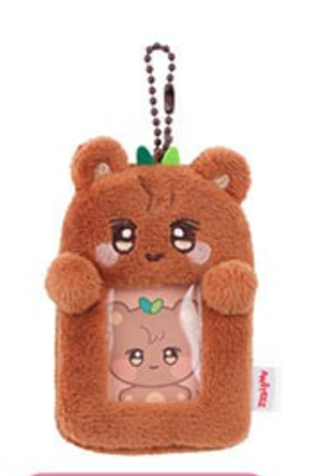 A brown plush bear-shaped card holder or phone case with a transparent window showing a cartoon character inside, attached to a dark bead keychain strap. A small white tag with red text is visible on the right side.