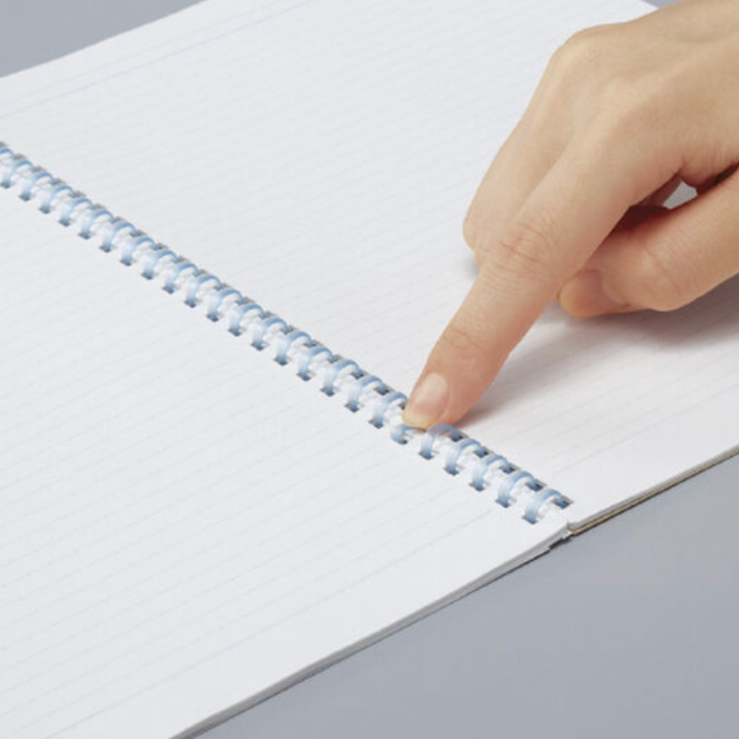 A close-up of a hand pointing at the spiral binding of a white lined notebook on a gray surface.