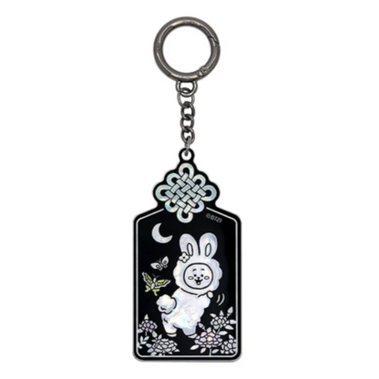 A black and silver keychain featuring a white cartoon bunny, a crescent moon, butterflies, and floral details, suspended from a silver metal ring on a plain white background.
