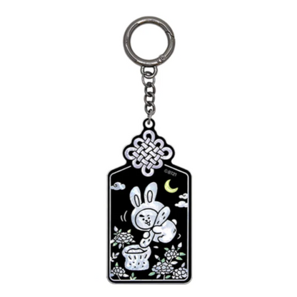 A black and silver keychain featuring a white cartoon bunny, a crescent moon, clouds, and floral details, suspended from a silver metal ring on a plain white background.