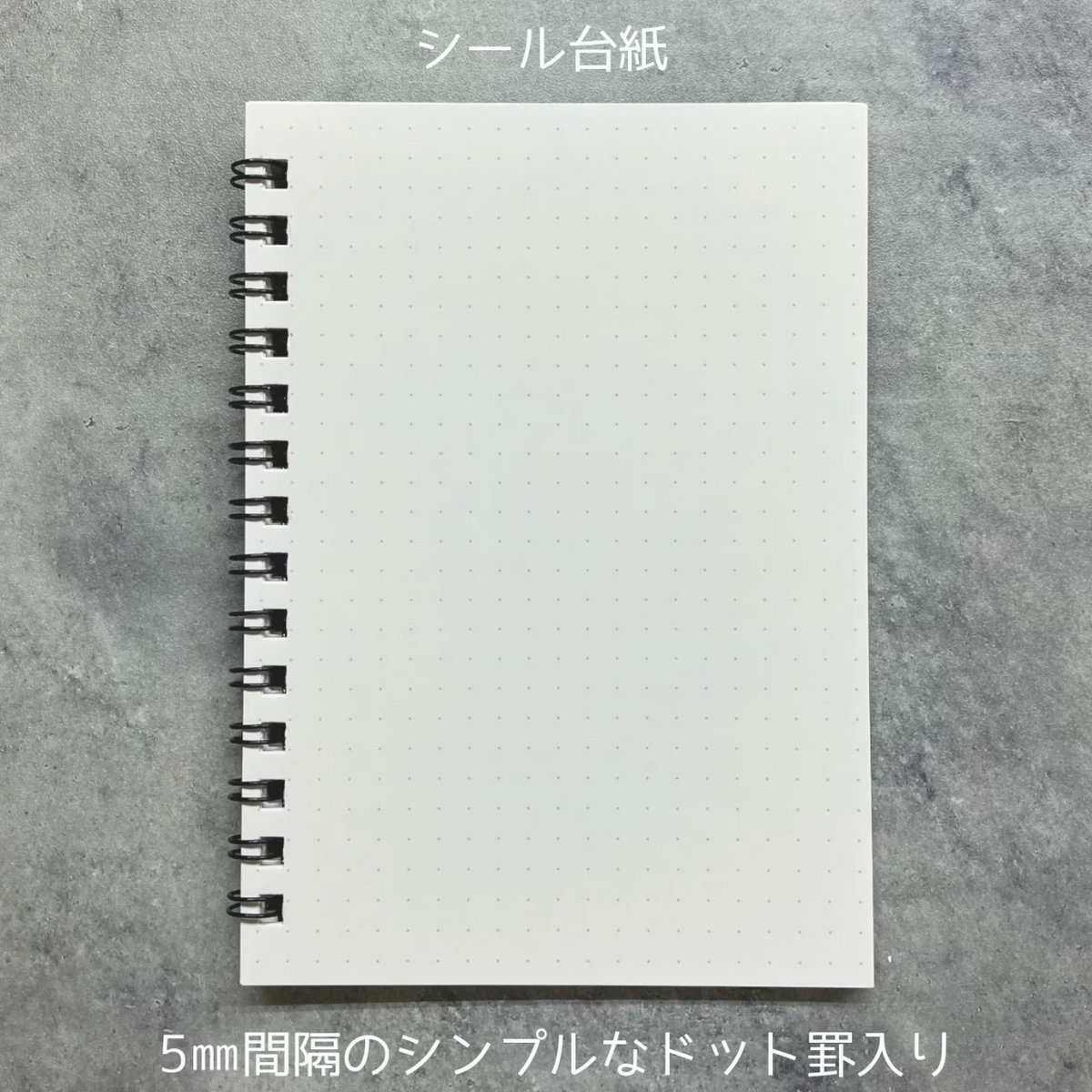 A white dotted sheet of paper with a black spiral binding, shown on a gray textured background with Japanese text above and below.
