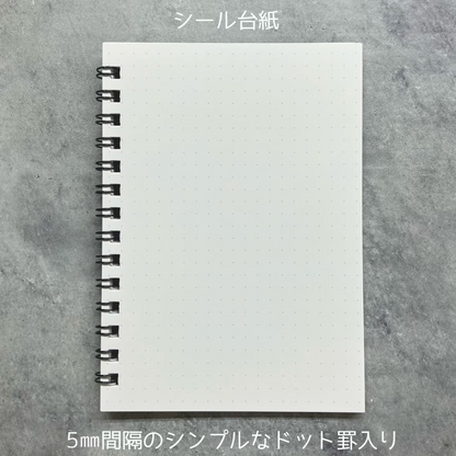 A white dotted sheet of paper with a black spiral binding, shown on a gray textured background with Japanese text above and below.