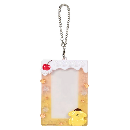 A Sanrio Pompompurin character acrylic keychain card holder with a yellow dog figure, a white whipped cream top with a red cherry, and a silver chain, shown on a white background with an label in the top left corner.