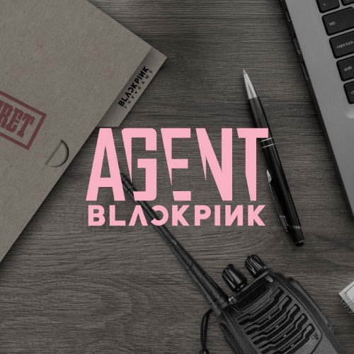 Tabletop scene with 'Agent Blackpink' text, walkie-talkie, pen, and laptop on a wooden surface.
